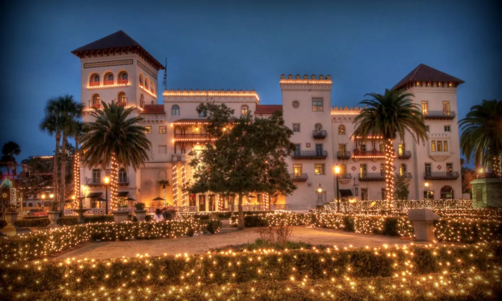 Mansion at night-time with palm trees filled with warm white holiday lights